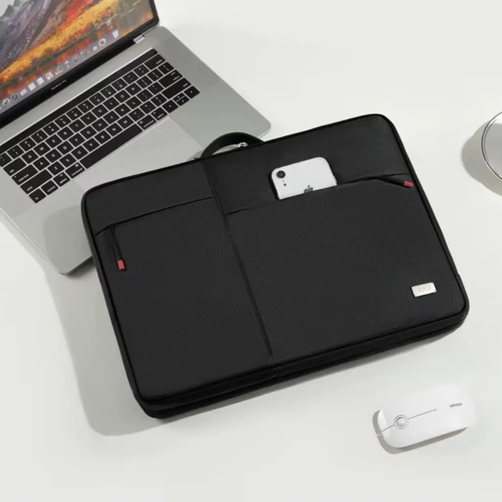 De laptoptas dames schokbestendig naast een MacBook laptop op een wit bureau, wat de perfecte pasvorm voor Apple apparaten toont. De externe zak met rode ritssluiting is zichtbaar voor het opbergen van een mobiele telefoon of andere kleine accessoires.