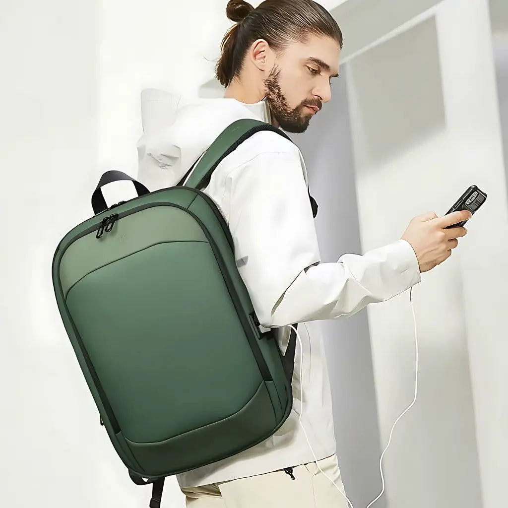 Man met een laptop rugzak 17 inch groen, aangesloten op een powerbank via de USB-oplaadpoort, ideal voor onderweg.