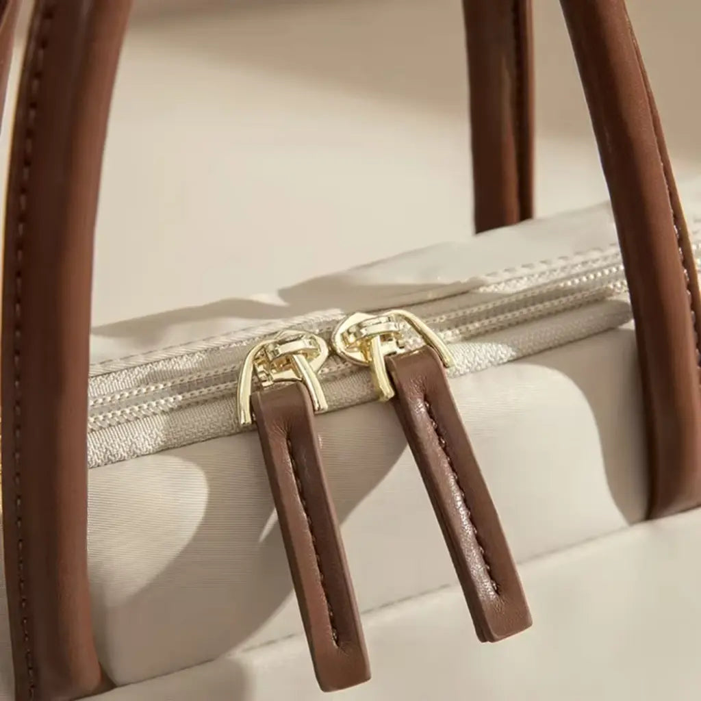 Close-up van de gouden ritssluiting op een beige laptoptas voor dames met bruine leren details.