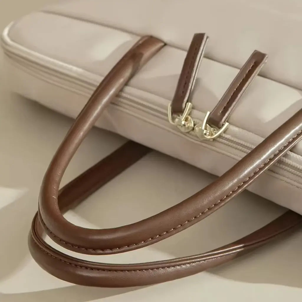 Detail van gouden hardware en bruine handvatten op een beige laptoptas voor dames.