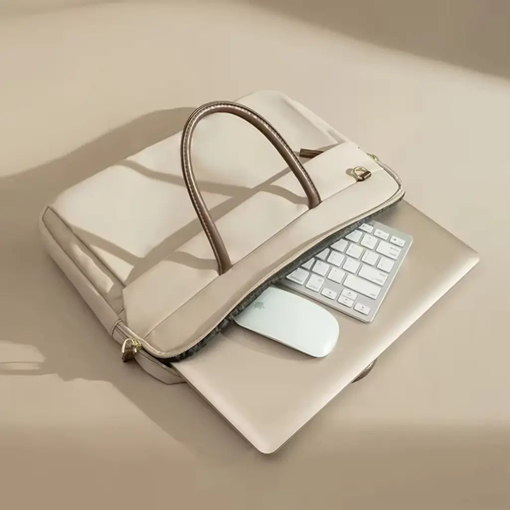 Beige laptoptas voor dames geplaatst op een zilveren laptop met toetsenbord en muis.
