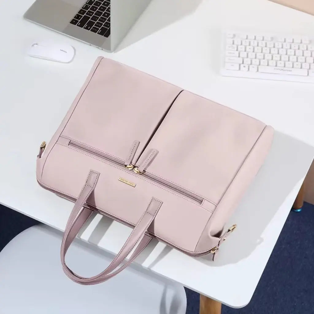 Een roze laptoptas dames 15.6 inch op een wit bureau met laptop en toetsenbord in een modern kantoor. De laptoptas dames 15.6 inch roze voegt een stijlvolle touch toe aan de werkplek en combineert functionaliteit met een verfijnd design.