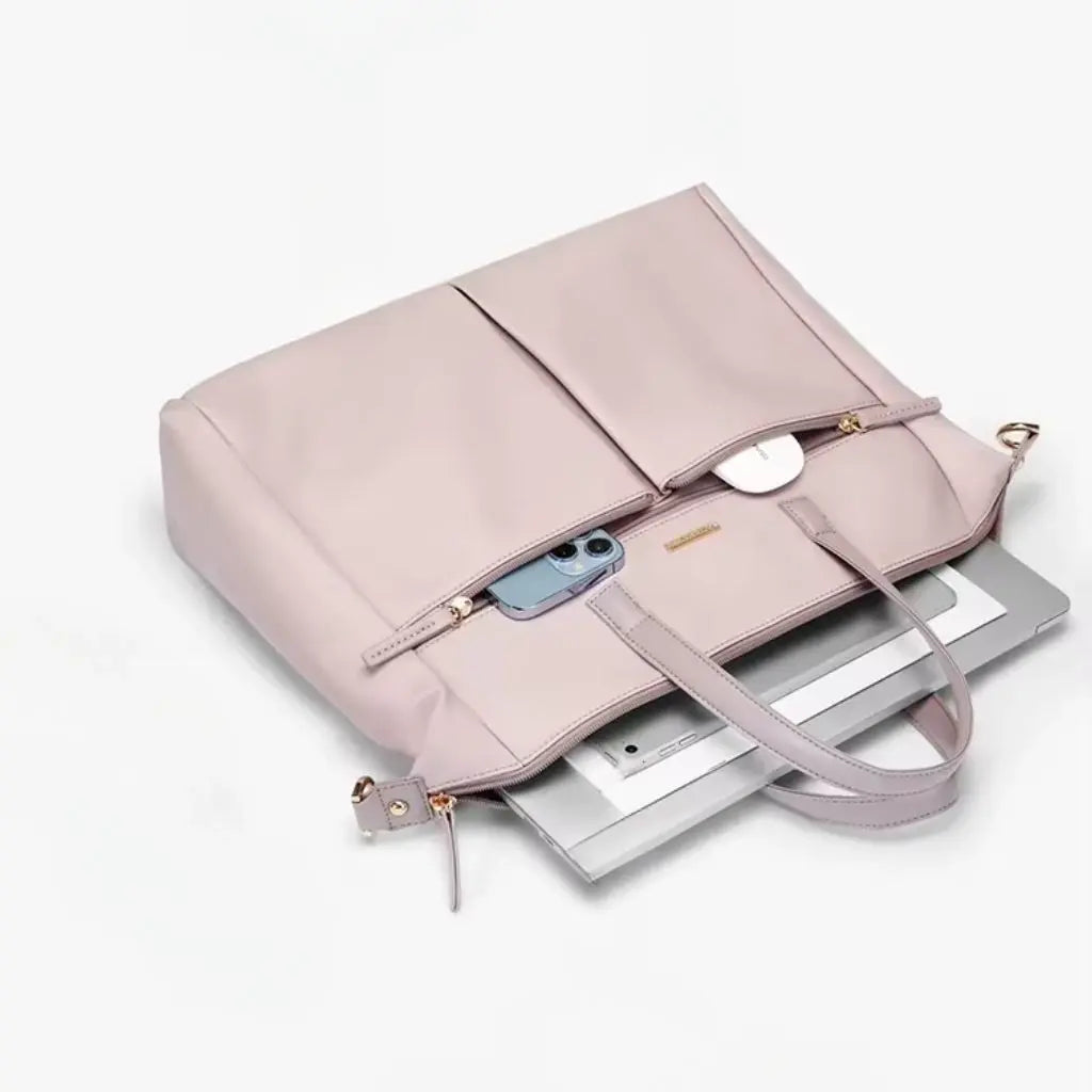 Bovenaanzicht van een roze laptoptas dames 15.6 inch op een wit bureau naast een laptop en accessoires. De laptoptas dames 15.6 inch roze past perfect in een minimalistisch kantoorinterieur en is praktisch voor het transporteren van werkbenodigdheden.