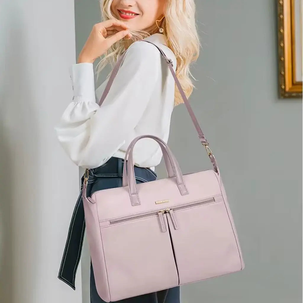 Vrouwelijk model draagt een roze laptoptas dames 15.6 inch als schoudertas met een chique witte blouse en donkere jeans. De laptoptas dames 15.6 inch roze accentueert de professionele look met een vleugje kleur, ideaal voor moderne professionals.